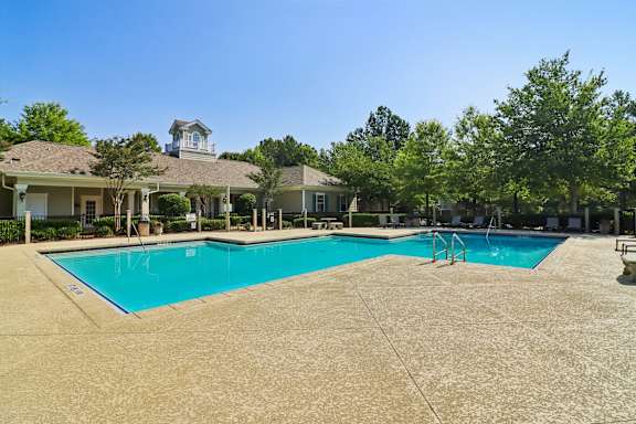 A large swimming pool in front of a house with a patio and trees.