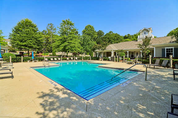 A large swimming pool surrounded by trees and a building in the background.