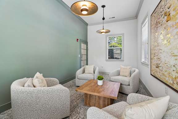 A living room with a grey sofa, a grey armchair, a grey chair, a wooden coffee table, a small potted plant, a white pillow, a painting, a window, a door, a wall, a ceiling