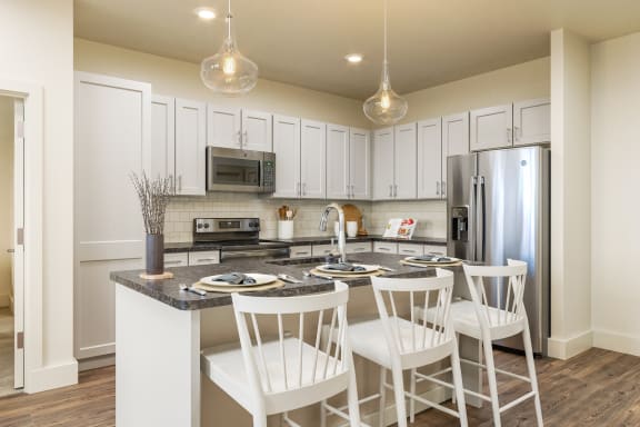 a kitchen with white cabinets and a large island with three white chairs at Livano Trinity Apartments, Nashville, Tennessee