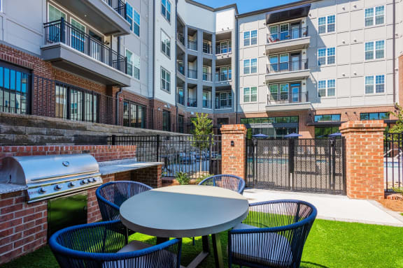 a patio with a table and chairs with an outdoor grill and an apartment building in the background at The Livano Tryon, Charlotte, North Carolina