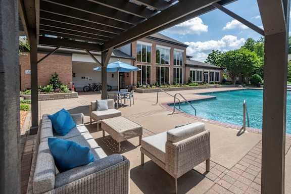 A patio with a couch and chairs under a roof next to a pool.