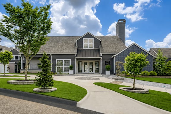 A large house with a grey roof and a chimney is surrounded by a well-manicured lawn and trees.