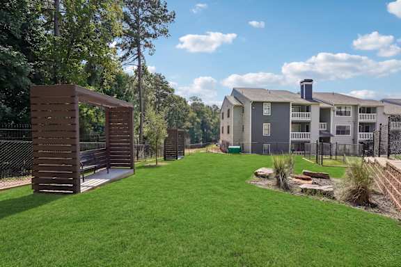 A grassy area with a wooden structure and apartment buildings in the background.