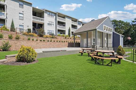 A small building sits in a grassy area in front of apartment buildings.