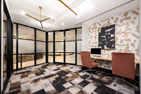 a room with a desk and chairs and a wall of windows