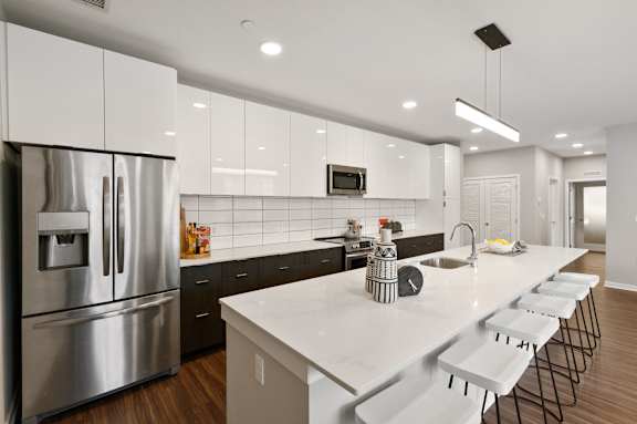 A modern kitchen with a long white counter and stainless steel appliances.
