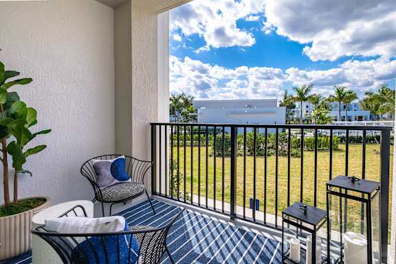 A balcony with a chair, table, and potted plant overlooking a grassy area.