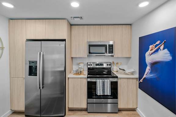 A modern kitchen with a refrigerator, microwave, oven, and a painting on the wall.