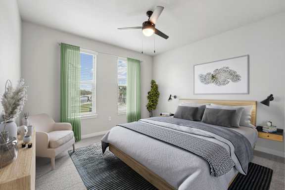 A bedroom with a large bed, a chair, a table, and a ceiling fan.