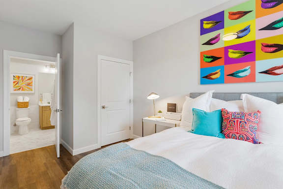 A bedroom with a bed, a desk, and a colorful artwork on the wall.