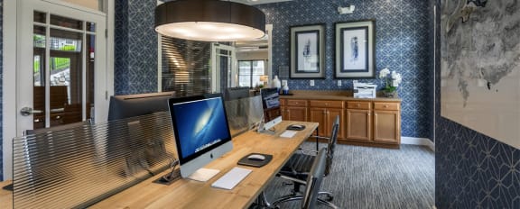 Business center with printed navy wall paper, framed images, and center wooden table with computers for resident use at Chesapeake Ridge, Maryland, 21901