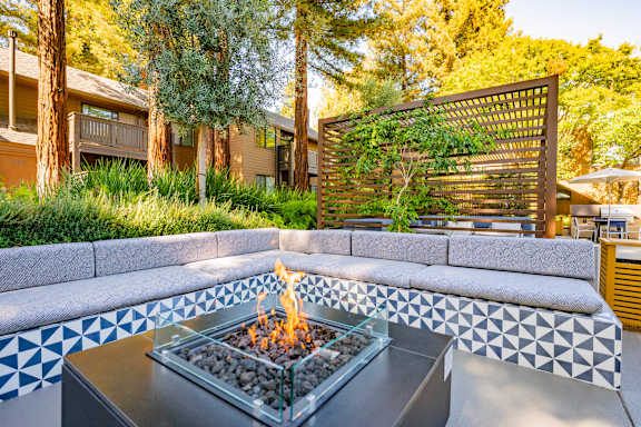 A fire pit in the middle of a patio surrounded by a white and black tiled bench.