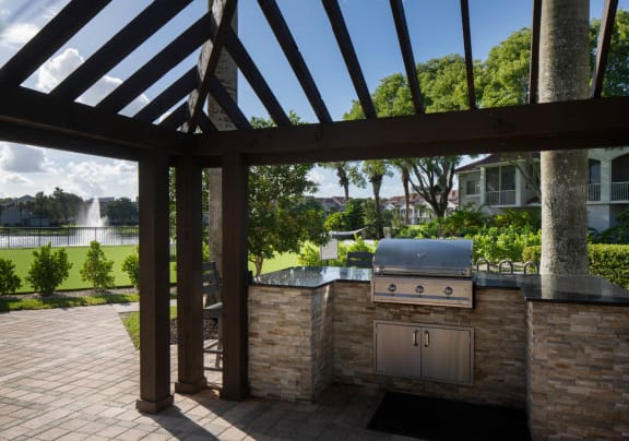 an outdoor kitchen with a grill and a pool in the background