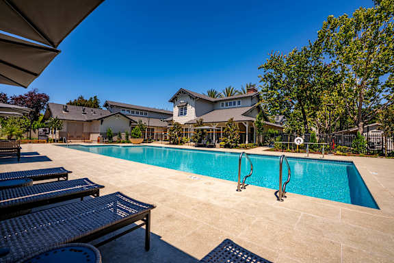 A large swimming pool with a slide and sun loungers in front of a house.
