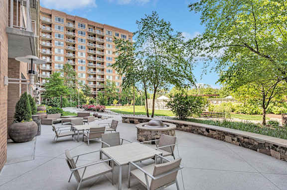 A patio with tables and chairs is surrounded by trees and a stone wall.