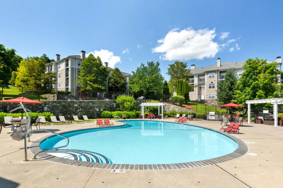 a swimming pool with red chairs and umbrellas and a building in the background
