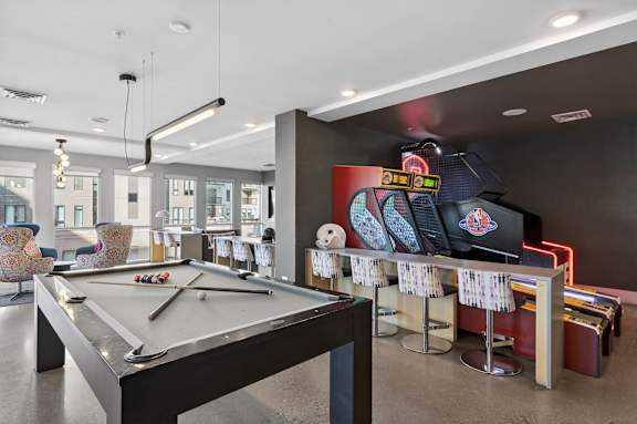 A pool table is in the middle of a room with a bar and chairs.