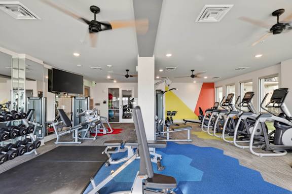 Apartment fitness center with modern gym equipment and large windows.