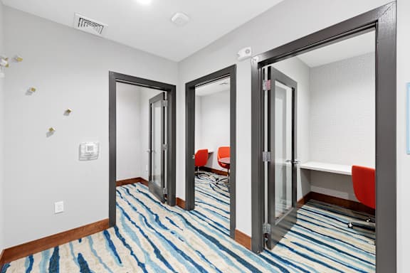 A hallway with a striped carpet and a row of red chairs.