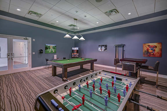 A foosball table is in the middle of a room with a pool table and a TV.