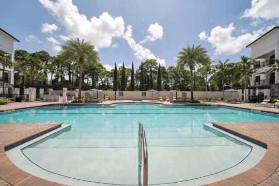 a large swimming pool with palm trees and apartments in the background