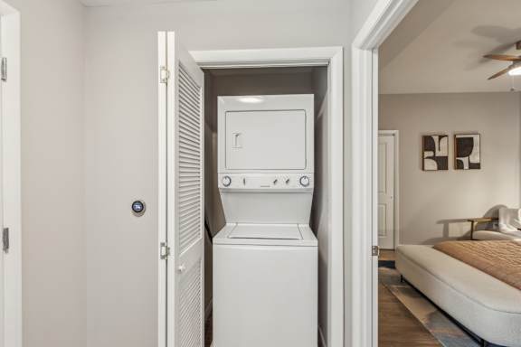 A white dryer is in a doorway between a bedroom and a hallway.