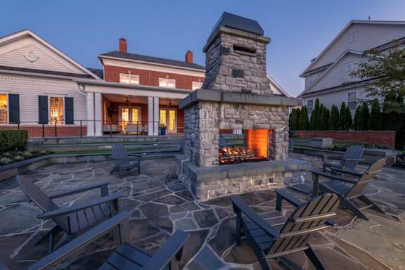 A stone fireplace is the centerpiece of a patio with chairs and tables.
