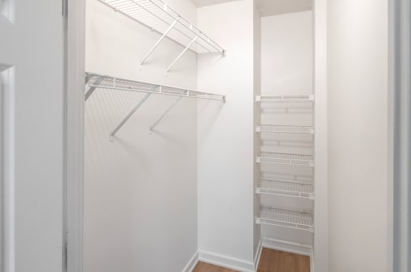a walk in closet with white walls and shelves and a mirrored closet door
