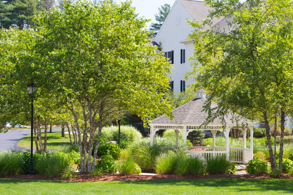 a white gazebo in a park with a house in the background