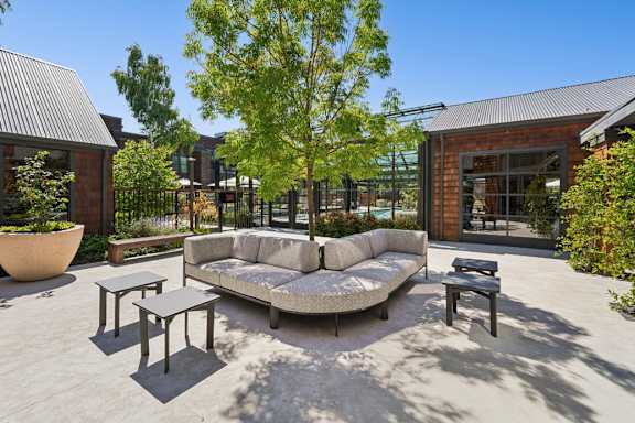 A patio with a couch, chairs, and a table with a tree in the background.