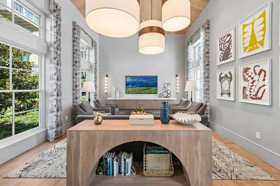 A living room with a large window, a grey sofa, a wooden coffee table, and a painting on the wall.