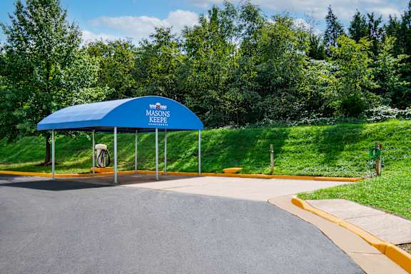 A blue canopy with a white sign that says "Masons Keep" is in front of a grassy area.