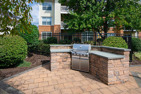 A brick BBQ grill is in the middle of a brick patio.