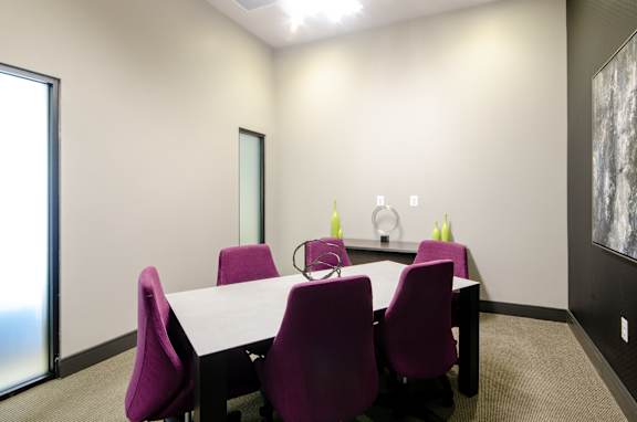 A conference room with a white table and purple chairs.