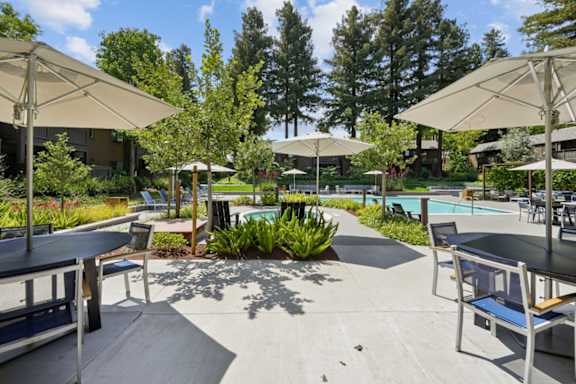 A pool area with tables and chairs and umbrellas.