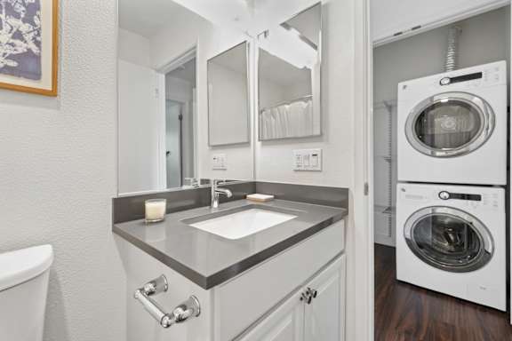 A modern bathroom with a white sink and a washing machine in the background.