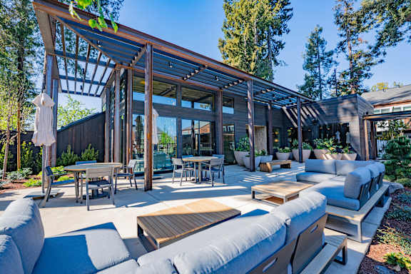 A modern outdoor seating area with a wooden pergola and grey couches.