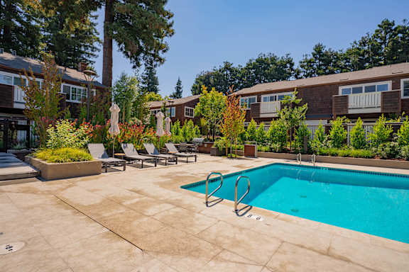 A pool surrounded by chairs and trees.