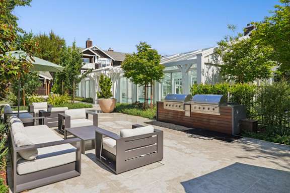 A patio with a table and chairs is surrounded by greenery.