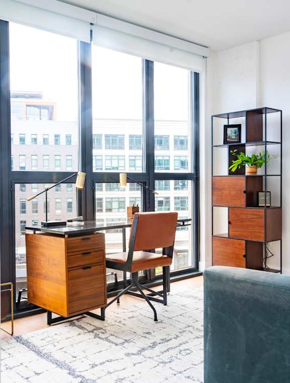 A room with a desk, chair, and a shelf with a potted plant.
