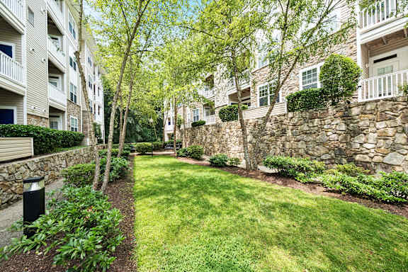 A stone wall separates a grassy area from apartment buildings.