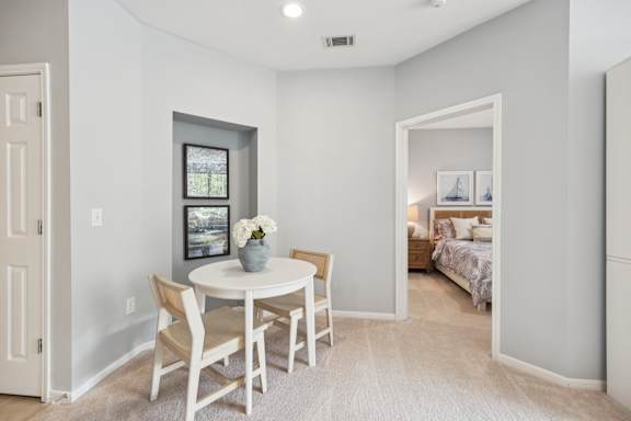 A white dining table with four chairs is in a room with a bedroom in the background.