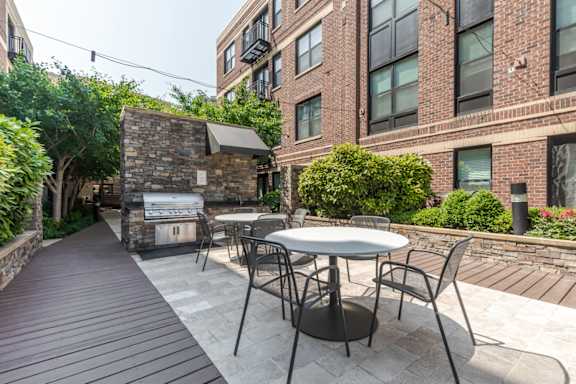 A patio with a table and chairs is surrounded by a brick wall and a tree.