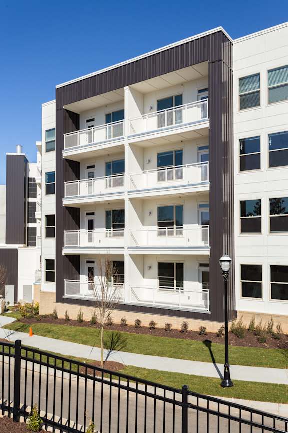 A modern apartment building with balconies and a black fence in front.