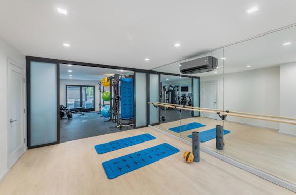 a gym with yoga mats and weights on the floor and a mirrored wall with a
