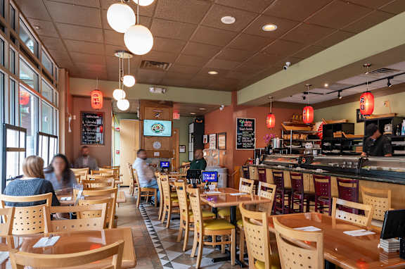A restaurant with wooden tables and chairs and people sitting at the tables.