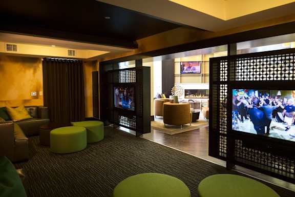 A room with a television and a screen with a picture of a horse riding show.