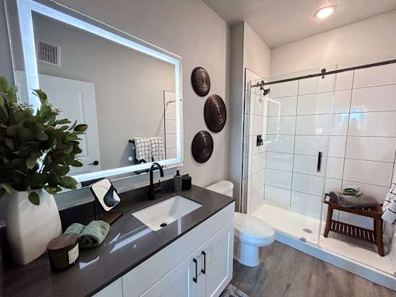 A bathroom with a sink, mirror, toilet, and shower.