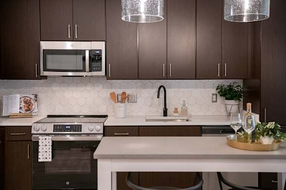 A modern kitchen with dark brown cabinets and a white backsplash.